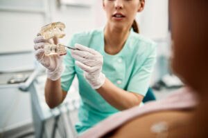 Close-up of orthodontist using dentures and explaining dental implants procedure to her patient at dentist's office.