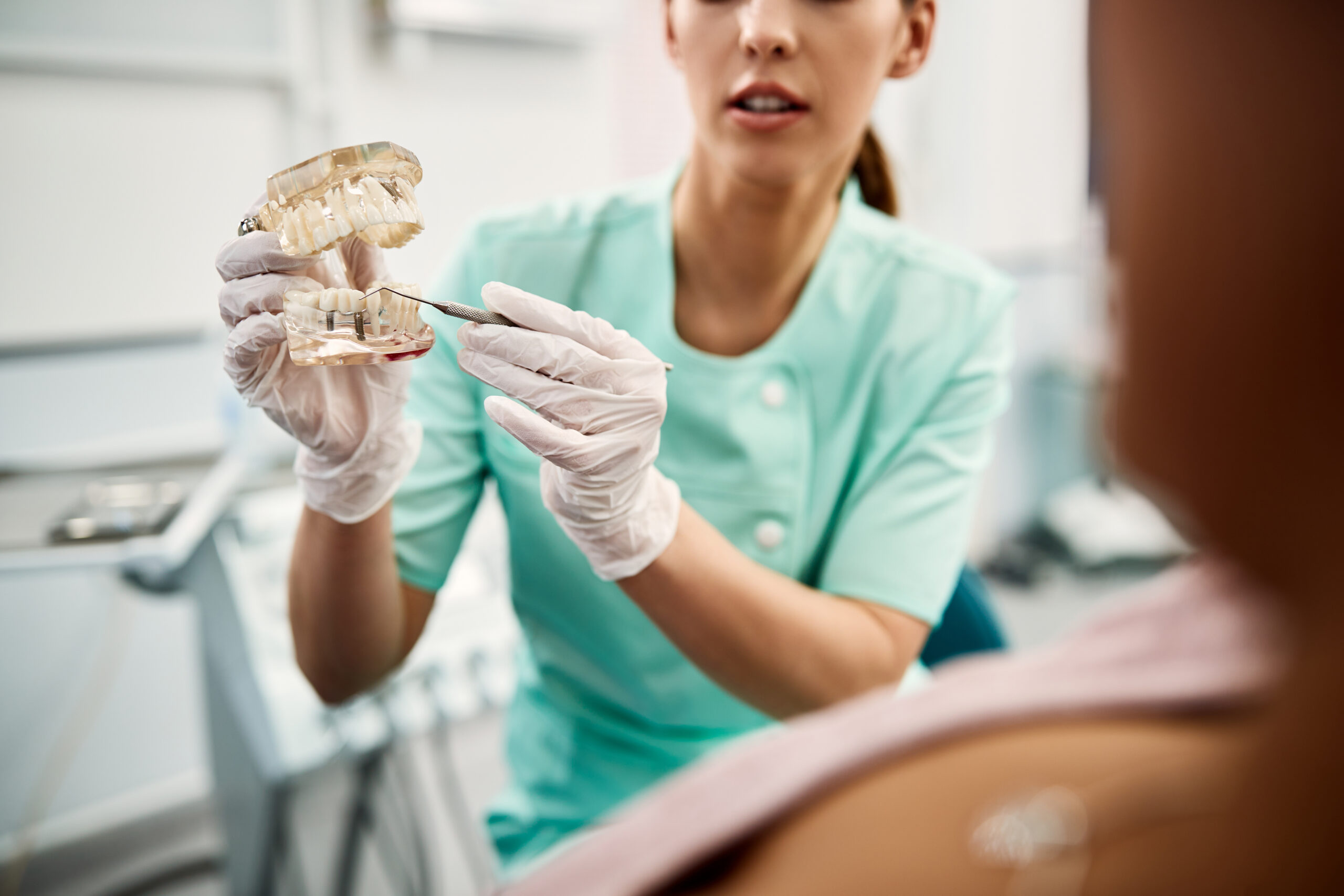 Close-up of orthodontist using dentures and explaining dental implants procedure to her patient at dentist's office.